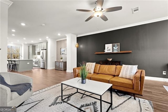 living area with crown molding, baseboards, visible vents, and light wood finished floors