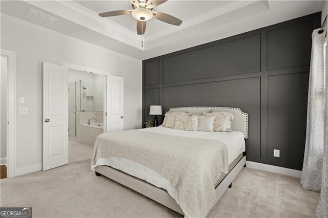 bedroom featuring visible vents, ensuite bath, light carpet, a raised ceiling, and a decorative wall