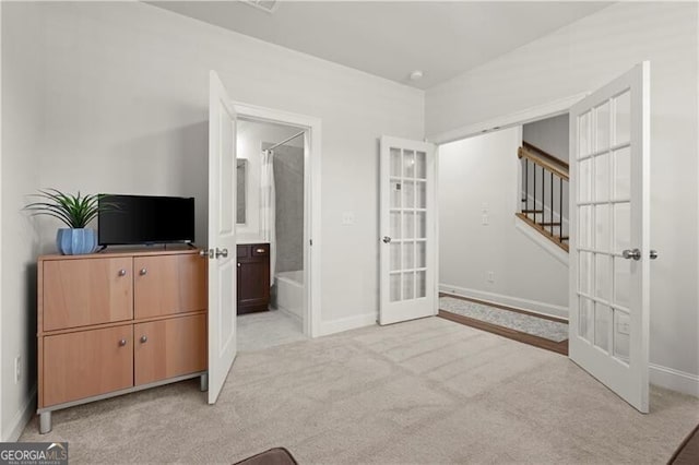 bedroom with french doors, baseboards, light colored carpet, and ensuite bath