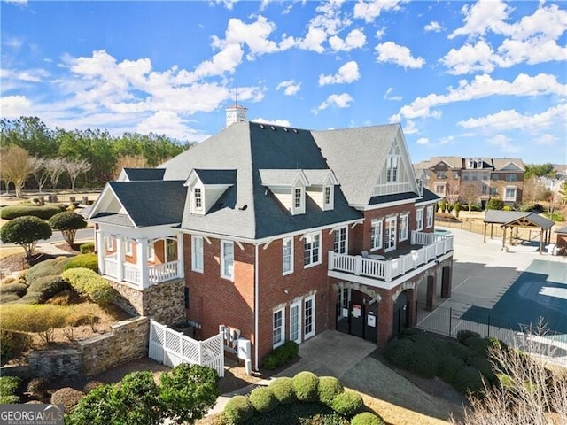 view of side of property featuring a balcony, fence, driveway, a chimney, and brick siding