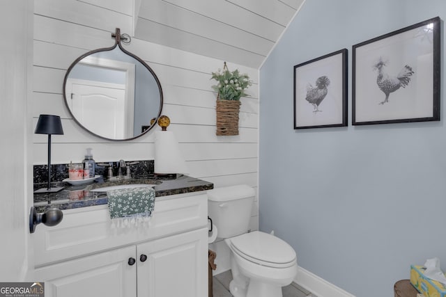 bathroom featuring baseboards, wood walls, toilet, vaulted ceiling, and vanity