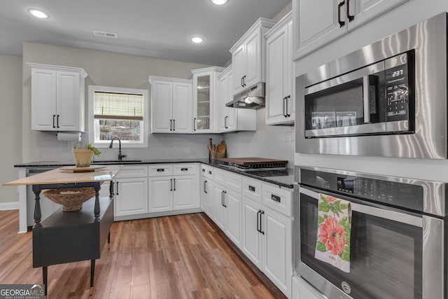 kitchen featuring visible vents, under cabinet range hood, dark countertops, wood finished floors, and stainless steel appliances