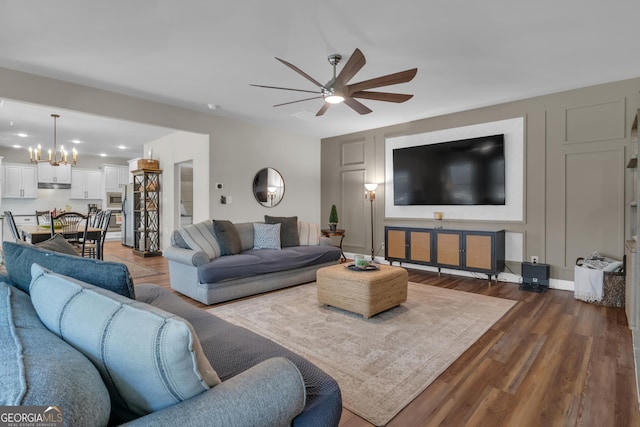 living area with dark wood-style floors, a decorative wall, and ceiling fan with notable chandelier