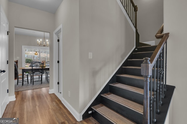 staircase with baseboards, wood finished floors, and a chandelier