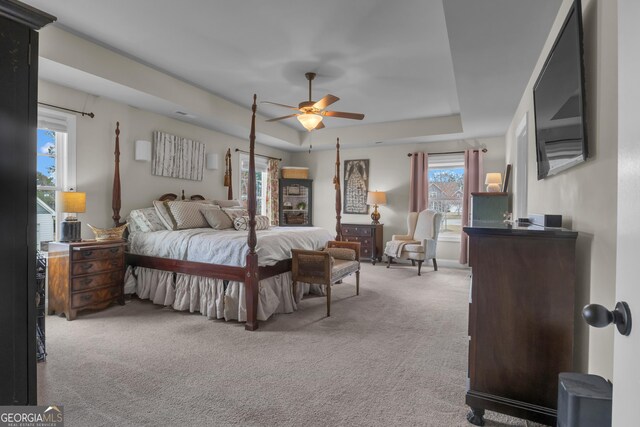 bedroom featuring a tray ceiling, light carpet, and ceiling fan