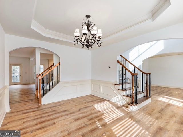 stairs featuring wood finished floors, a wainscoted wall, a tray ceiling, crown molding, and a decorative wall