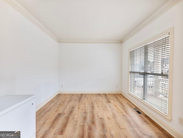 spare room with light wood finished floors, crown molding, visible vents, and baseboards
