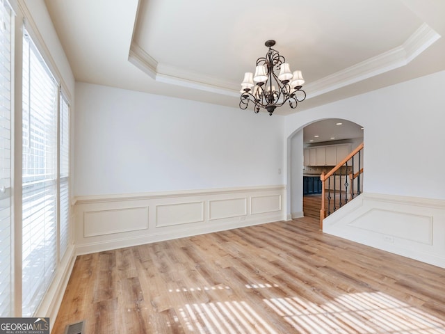 empty room featuring stairway, wood finished floors, visible vents, a raised ceiling, and a notable chandelier