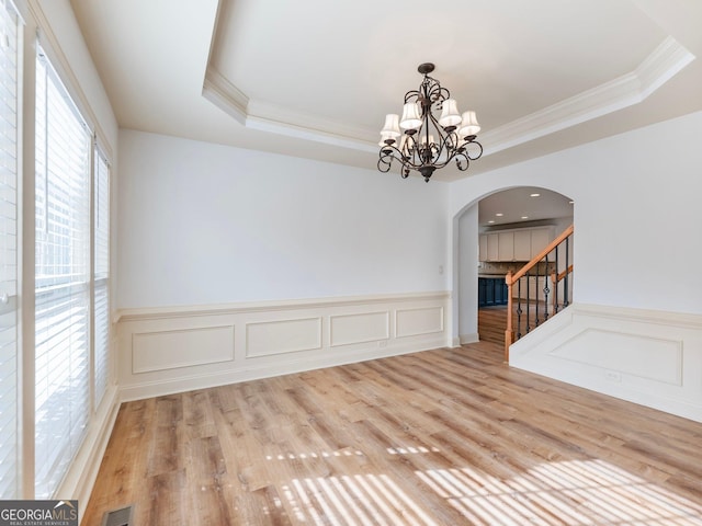 unfurnished dining area featuring arched walkways, a raised ceiling, ornamental molding, and a chandelier