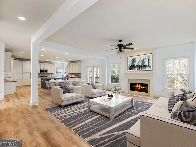 living room featuring a warm lit fireplace, recessed lighting, light wood-style flooring, and ceiling fan