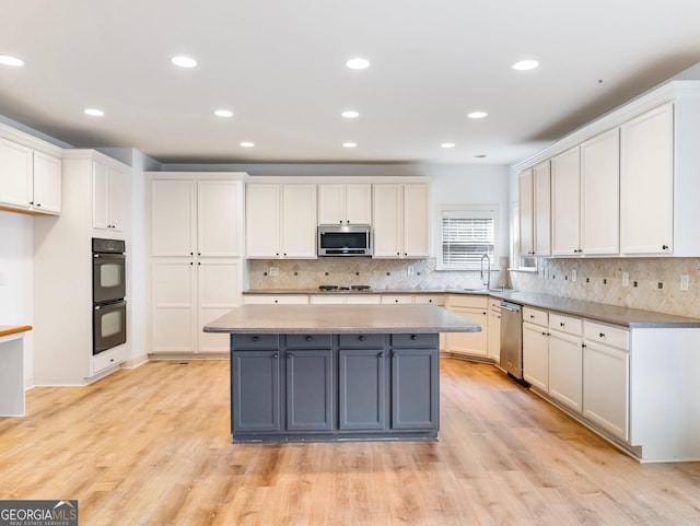 kitchen with a kitchen island, a sink, white cabinets, appliances with stainless steel finishes, and light wood-type flooring