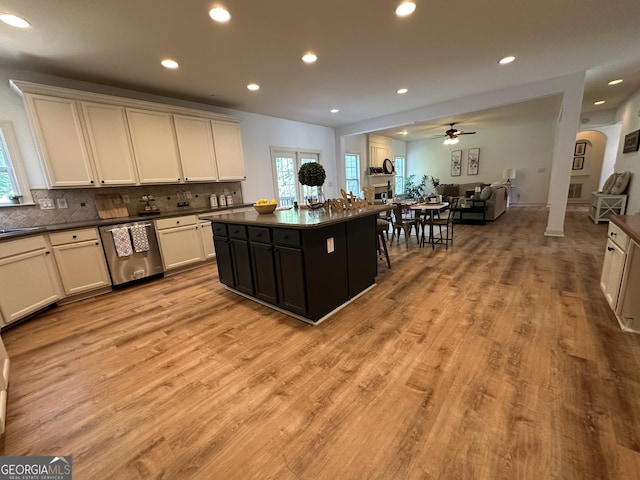 kitchen with light wood-type flooring, open floor plan, a ceiling fan, stainless steel dishwasher, and dark countertops