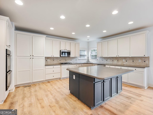 kitchen featuring tasteful backsplash, a center island, light wood-style floors, appliances with stainless steel finishes, and white cabinets