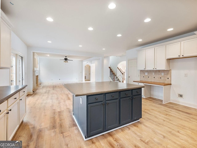 kitchen featuring dark countertops, backsplash, light wood-style floors, arched walkways, and white cabinets