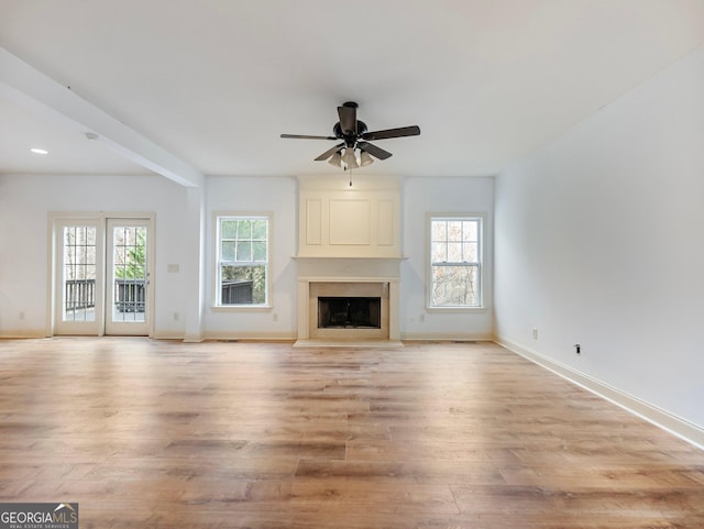 unfurnished living room with plenty of natural light, baseboards, ceiling fan, and light wood-style floors