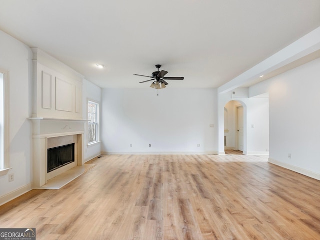 unfurnished living room featuring a ceiling fan, light wood-type flooring, baseboards, arched walkways, and a large fireplace