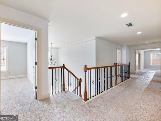 hall featuring visible vents, an upstairs landing, carpet, and baseboards