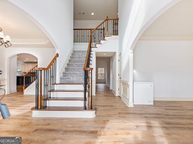 stairs featuring crown molding, a towering ceiling, recessed lighting, and wood finished floors
