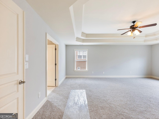 empty room with a raised ceiling, light colored carpet, baseboards, and ceiling fan