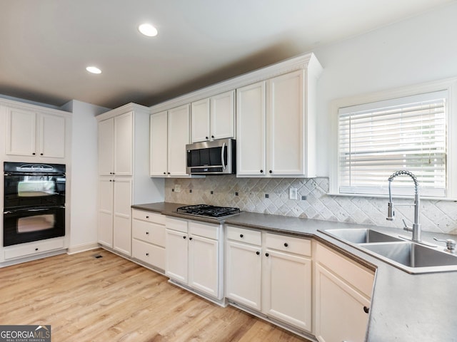kitchen featuring light wood finished floors, a sink, stainless steel appliances, white cabinets, and backsplash