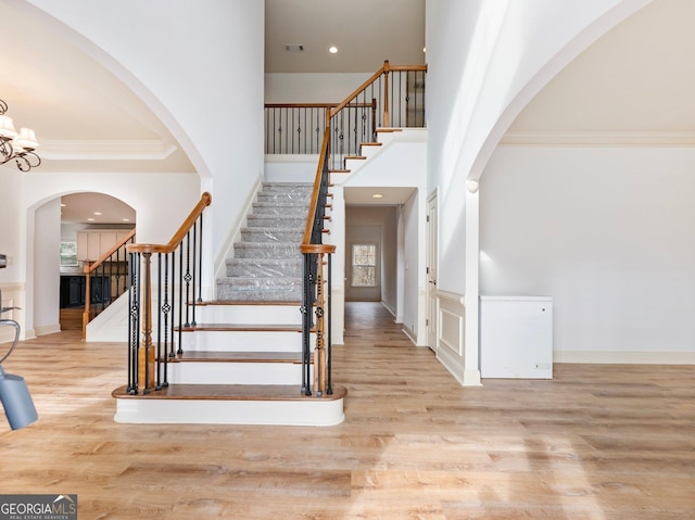 stairway featuring visible vents, ornamental molding, wood finished floors, a high ceiling, and an inviting chandelier