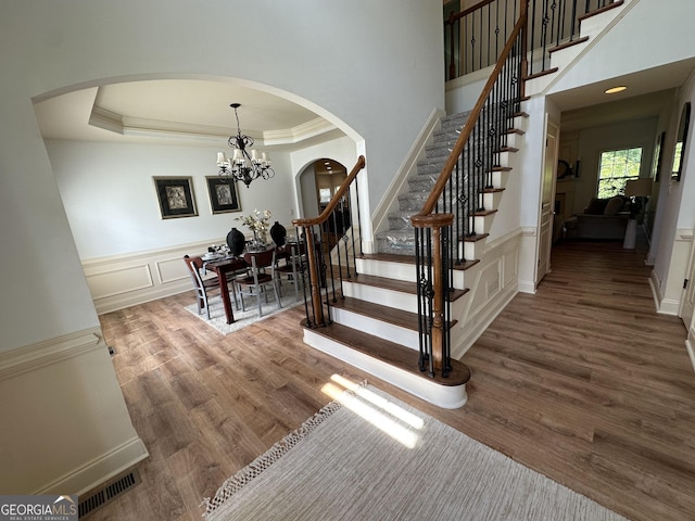 stairway with wood finished floors, a decorative wall, arched walkways, a chandelier, and ornamental molding