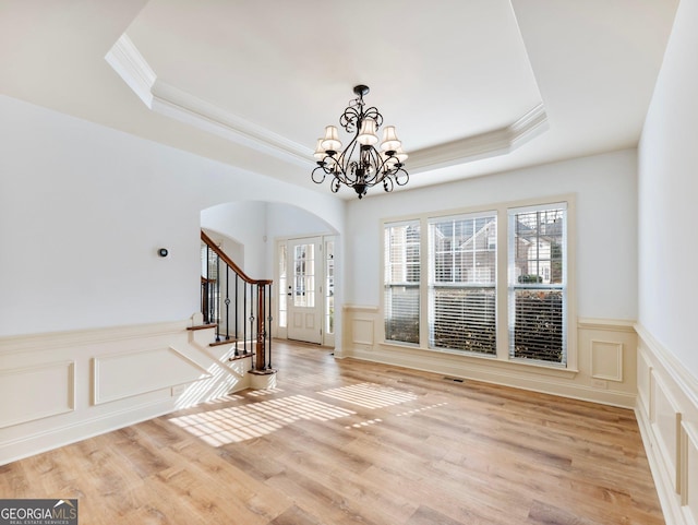 entryway featuring a tray ceiling, stairway, light wood-style floors, and arched walkways