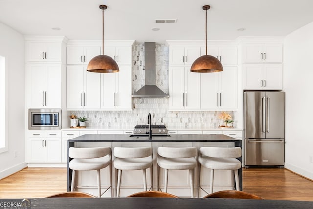 kitchen with decorative backsplash, appliances with stainless steel finishes, a kitchen island with sink, and wall chimney range hood