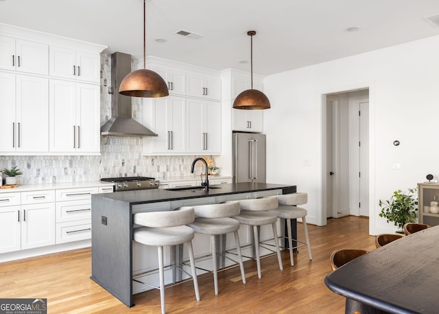 kitchen with visible vents, wall chimney range hood, a center island with sink, stainless steel appliances, and a sink