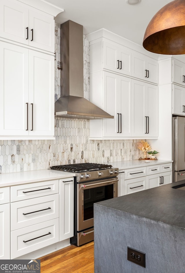 kitchen featuring light wood-type flooring, decorative backsplash, stainless steel appliances, white cabinetry, and wall chimney exhaust hood