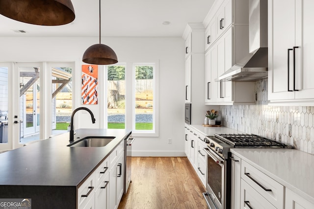 kitchen featuring visible vents, light wood-style flooring, stainless steel appliances, a sink, and wall chimney exhaust hood