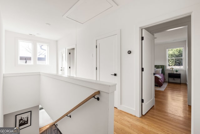 hallway with an upstairs landing, attic access, light wood-type flooring, and baseboards