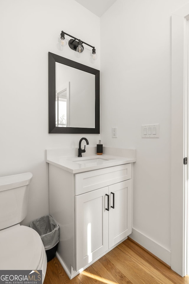 bathroom featuring baseboards, toilet, wood finished floors, and vanity