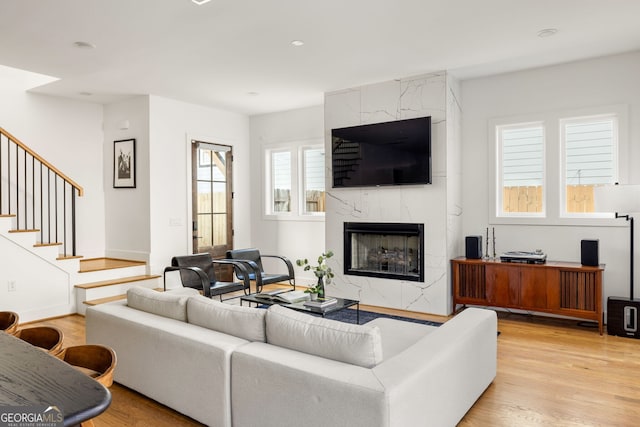 living area featuring light wood-type flooring, baseboards, a premium fireplace, and stairs