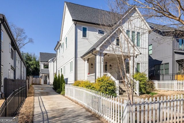 view of front facade featuring a fenced front yard, a residential view, driveway, and roof with shingles