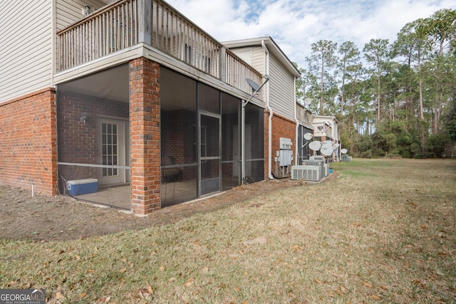 view of property exterior featuring a balcony, a lawn, brick siding, and a sunroom