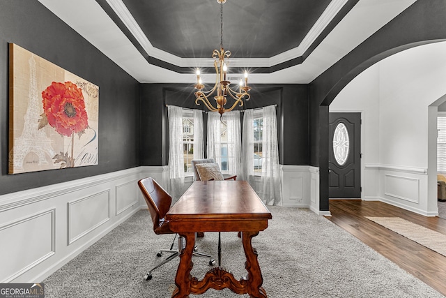 interior space featuring a tray ceiling, a decorative wall, arched walkways, and a chandelier