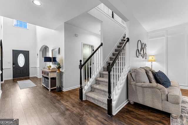 entrance foyer with dark wood finished floors, arched walkways, stairs, and baseboards