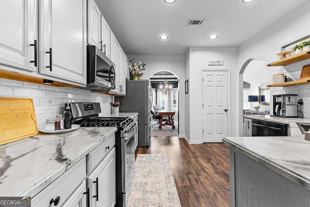 kitchen featuring dark wood-style flooring, light stone counters, arched walkways, and appliances with stainless steel finishes