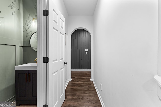 hallway featuring dark wood finished floors, arched walkways, baseboards, and a sink