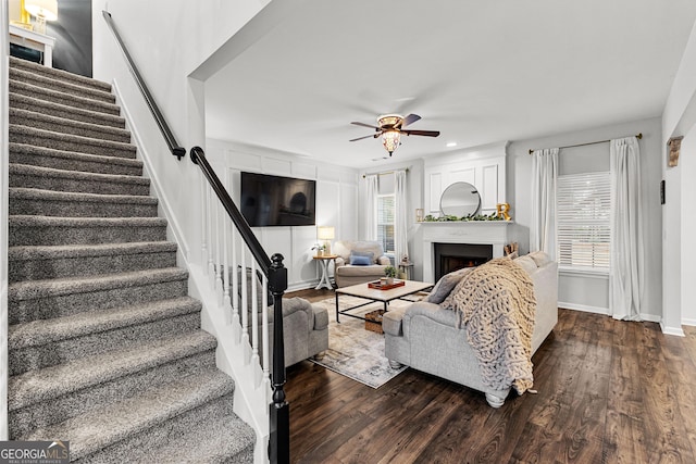 living area featuring dark wood-style floors, baseboards, a fireplace, ceiling fan, and stairs