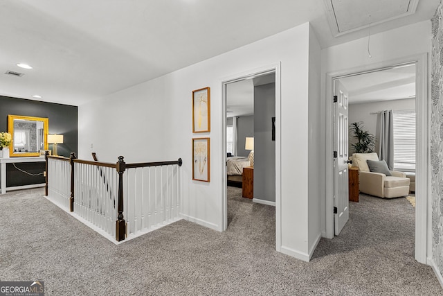 hall with attic access, an upstairs landing, carpet, and visible vents