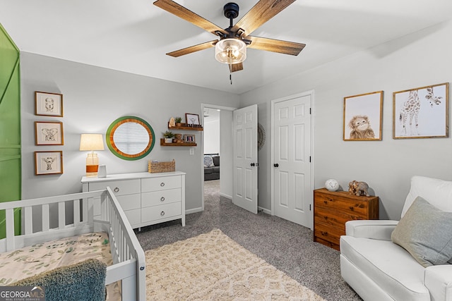 carpeted bedroom with a crib, baseboards, and ceiling fan