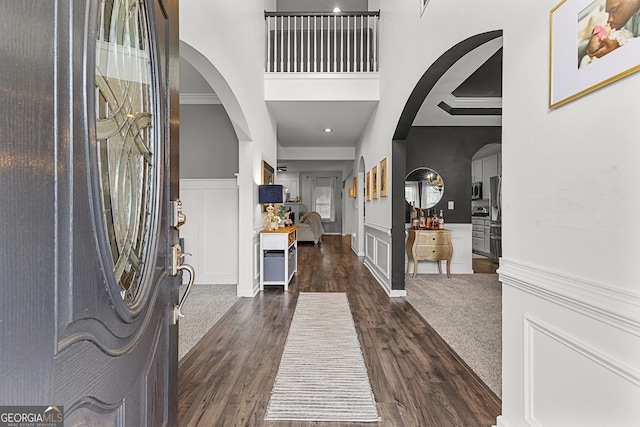 foyer featuring arched walkways, a decorative wall, and ornamental molding