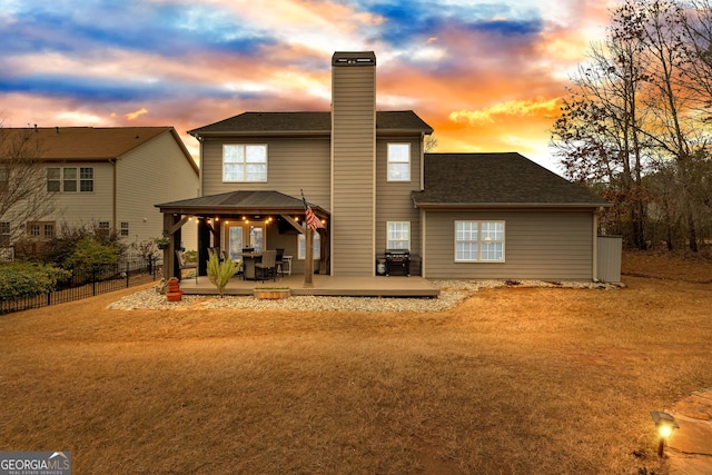 rear view of property featuring fence, a gazebo, a lawn, a chimney, and a deck