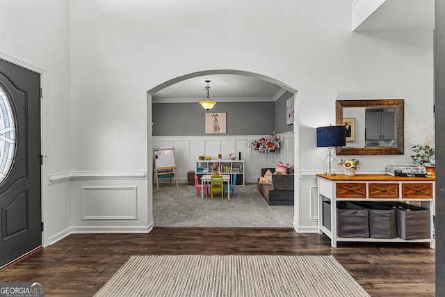 entryway featuring a wainscoted wall, arched walkways, wood finished floors, and ornamental molding