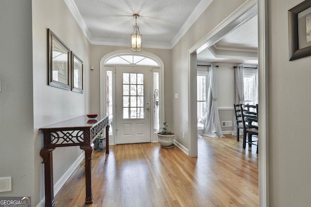 entrance foyer with visible vents, ornamental molding, a textured ceiling, wood finished floors, and baseboards