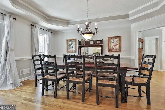 dining room featuring visible vents, light wood-style flooring, a raised ceiling, and ornamental molding