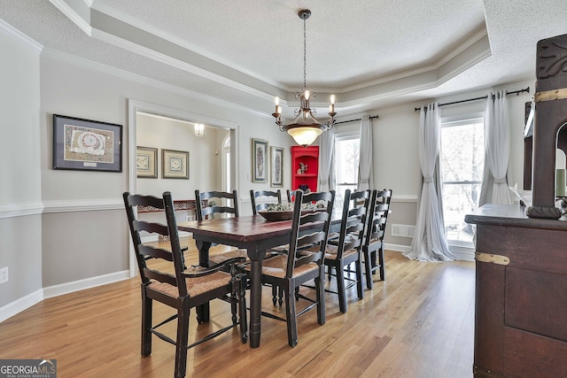 dining area with light wood-style flooring, crown molding, and a raised ceiling