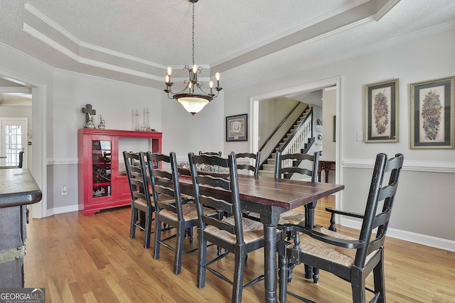 dining room with baseboards, ornamental molding, light wood-style flooring, a textured ceiling, and a raised ceiling